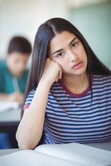 Portrait of sad schoolgirl sitting in classroom