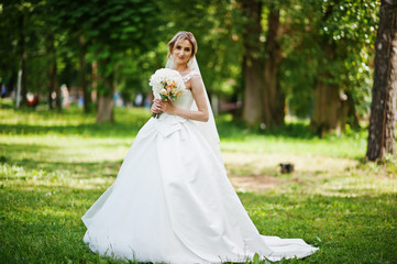 Fototapeta na wymiar Cute blonde bride with wedding bouquet at park on sunny day.