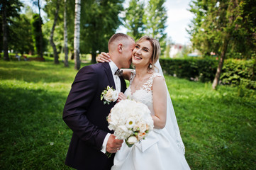 Fashionable wedding couple hugging at green park on sunny wedding day.