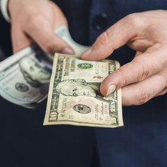 Male hand gives one ten dollars banknote, close-up view, business and finance concept.