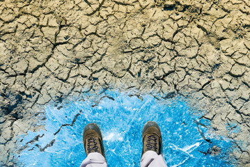 Climate change concept, man in dirty shoes stands on ice surface melted by desert