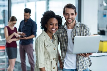 Portrait of smiling business executives discussing over laptop