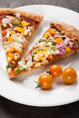 Vegetarian Pizza topped with tomatoes, onion, zucchini, and bell peppers on dark wooden background slightly above shot