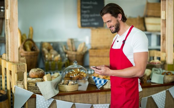 Smiling bakery staff using mobile phone at counter