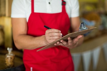 Mid section of bakery staff writing on clipboard at counter