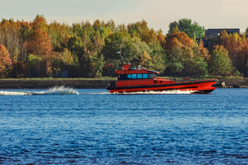 Red pilot ship moving past the autumn trees in Europe