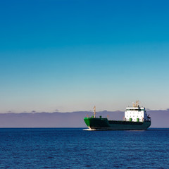 Fototapeta premium Green cargo ship moving in still water of Baltic sea