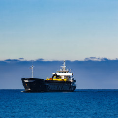 Black cargo ship with long reach excavator moving by baltic sea
