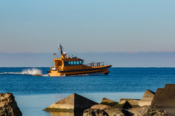 Yellow pilot ship moving at speed past the breakwater dam
