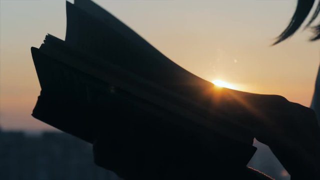 A girl is reading a book on the windowsill at sunset. Close up to hands.