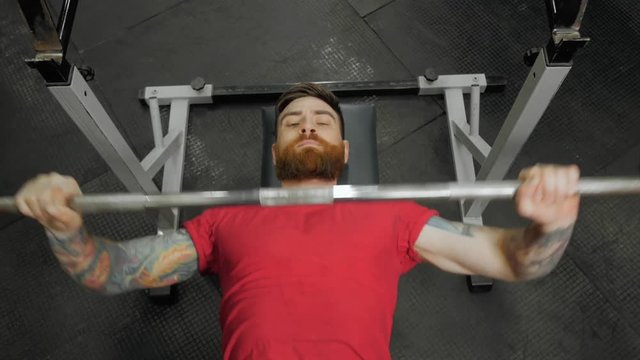 Young man lifting the barbell in the gym portrait. Steadycam follow shot of male athlete with brutal beard