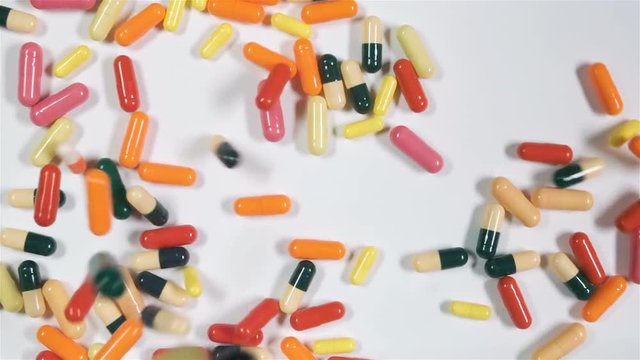 A huge number of pills falling on white background top view in slow motion. Multi-colored tablets are flying slowly in the air. A first aid kit. Beautiful drop pills on the table POV. Medicine chest.