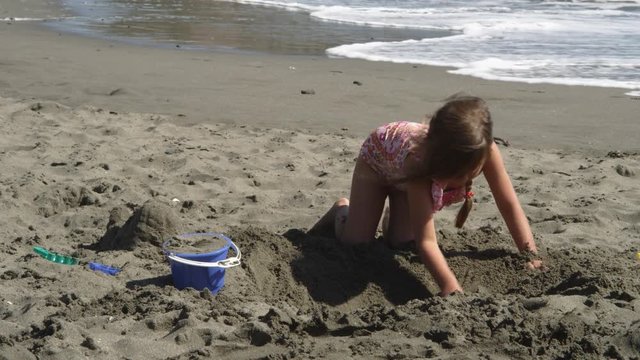 A little girl digging in the sand on a beach with surf in background