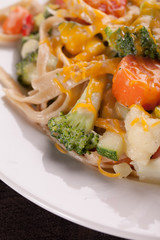 Vegetable Primavera with white sauce and shredded cheese with corn on the cob and slice of watermelon close up shot