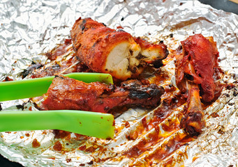 Nylon-tong is holding tandoori chicken on aluminium foil