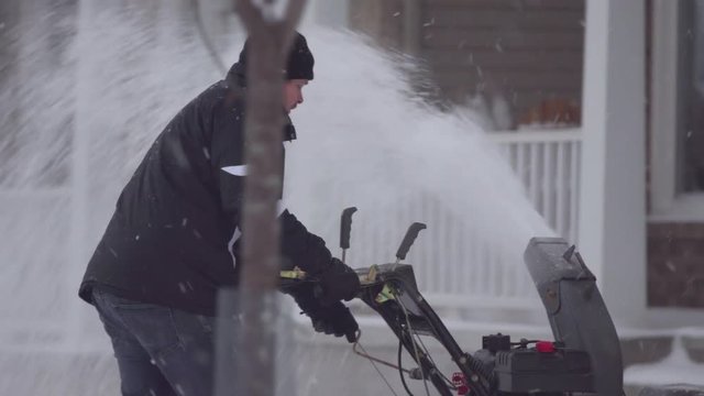 A close-up shot of a man snow-blowing his driveway during a heavy snowfall.