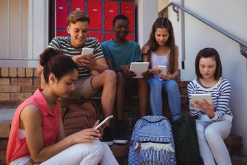 Students using mobile phone and digital tablet on staircase