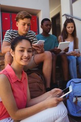 Students using mobile phone and digital tablet on staircase