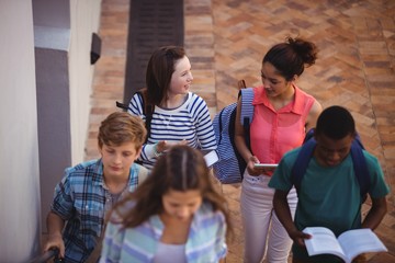 Students holding books and digital tablet walking through school campus