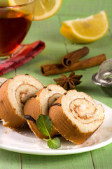Biscuit swiss roll with a cup of tea on green wooden background