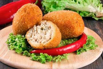three fried breaded cutlet with lettuce on a cutting board dark wooden background
