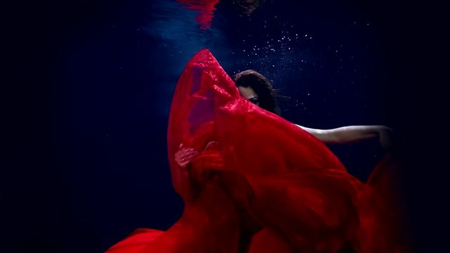 Flight in weightlessness of the underwater world of the young beautiful girl in elegant red dress.