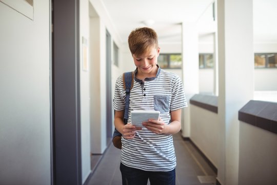 Happy schoolboy using digital tablet in corridor
