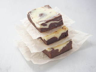 Marble chocolate brownie cheesecake arranged upon parchment. Homemade cake as food background. Selective focus on the front.