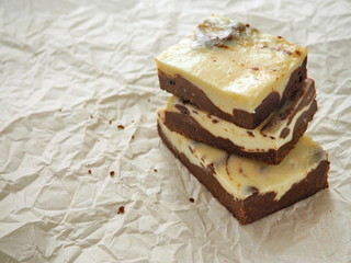 Stack of freshly baked brownie cheesecake. Homemade cake as food background. Marble chocolate brownies arranged upon parchment. Selective focus on the front.