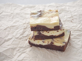 Stack of freshly baked brownie cheesecake. Homemade cake as food background. Marble chocolate brownies arranged upon parchment. Selective focus on the front.