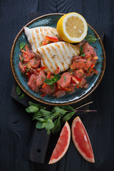 Plate with grilled calamari and grapefruit salad on a black wooden background, high angle view