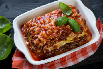 Close-up of italian lasagna bolognese in a white baking dish, selective focus
