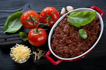 Freshly made bolognese sauce with green basil leaves, tomatoes, garlic and parmesan, studio shot on a black wooden background