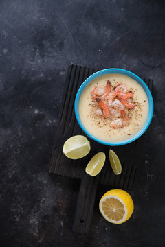 Top view of potato cream-soup with king shrimps on a dark stone background, copyspace