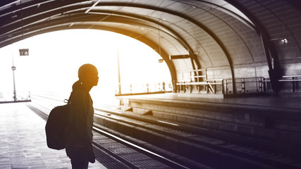 Silhouette for tourist girl backpacker waiting for train at the open station, travel abstract