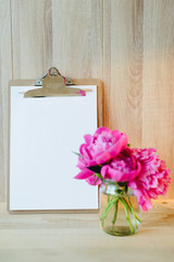 blank clipboard and pink peony bouquet in wooden interior