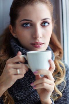 Young pretty woman in wool sweater with white coffee cup in hands