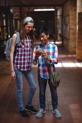 Classmates using mobile phone in corridor at school