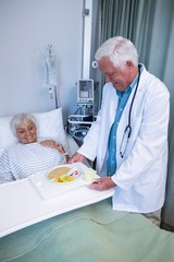 Doctor serving breakfast and medicine to senior patient