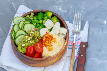 Bowl of bright healthy vegan lunch: vegetable salad with tofu, hummus and guacamole. Buddha rainbow wooden bowl, vegan concept.