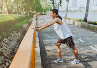 Young man stretching bodies, warming up for jogging in public park.