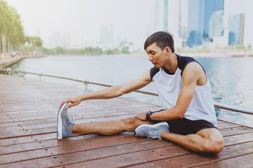 Young man stretching bodies, warming up for jogging in public park.