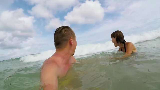 Happy Couple Waving And Swimming In Ocean. Honeymoon having fun in the ocan with big waves. Tropical island Bali, Indonesia. Slow motion.