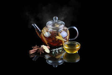 Glass teapot with black tea. Cinnamon, ginger, honey. On a black background with reflection