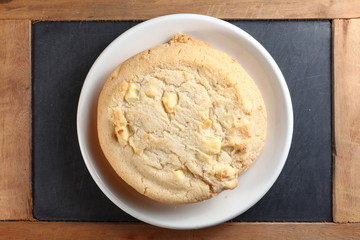 The white chocolate chip cookie on white dish put on slate board represent the pastry and bakery snack concept related idea.
