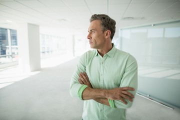 Business executive standing with arms crossed in office corridor
