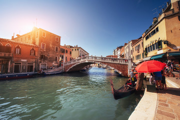 Green water channel with gondolas and colorful facades of old medieval buildings in the sun in Venice
