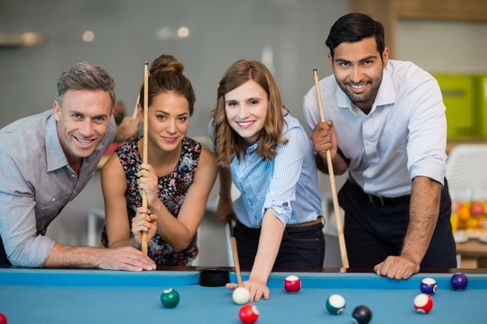 Smiling business colleagues playing pool in office space