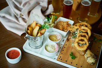 Photo Food set to beer: slices and potato wedges with ketchup mustard mayonnaise sauce pickles and sauerkraut with a beer glass on wooden backdrop, roast knuckle, sausages and burger.