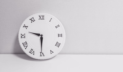 Closeup white clock for decorate show half past nine o'clock or 9:30 a.m. on white wood desk and wallpaper textured background in black and white tone with copy space